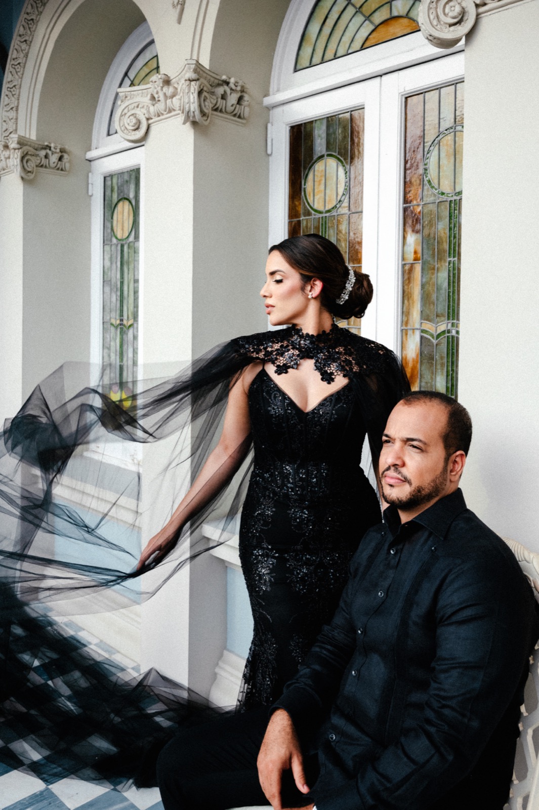 Camila y Hector vestidos de negro junto a los vitrales